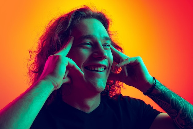 Portrait of young man posing smiling isolated over gradient red orange background in neon light