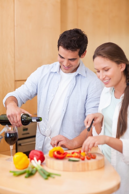 Portrait of a young man pouring a glass of wine while his wife is cooking