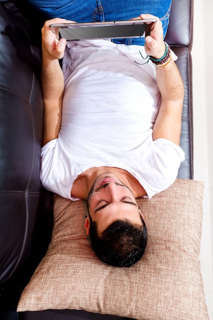 Portrait of a young man relaxing on a couch with a tablet.
