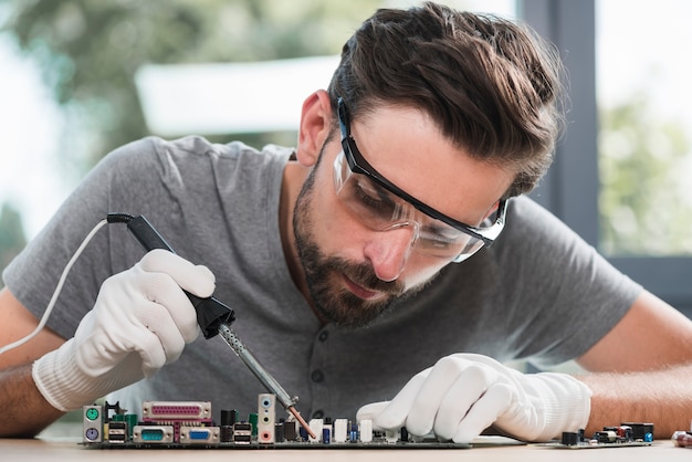 Portrait of a young man soldering computer circuit in workshop