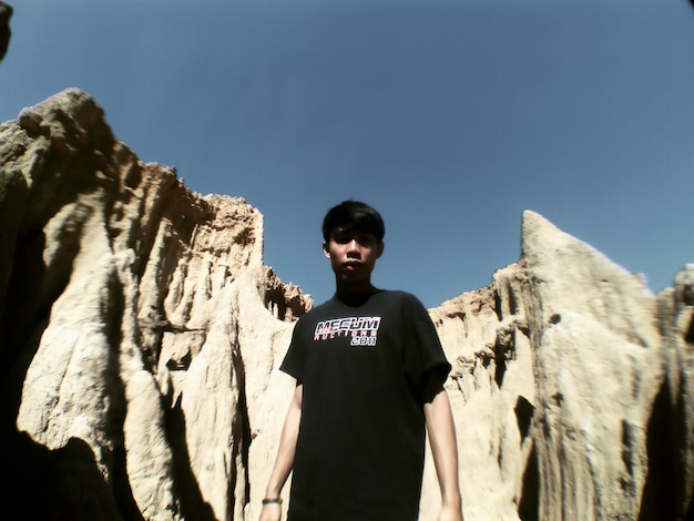 Photo portrait of young man standing at rock formation against clear blue sky