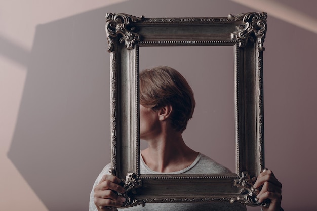 Portrait young man standing with picture frame at studio