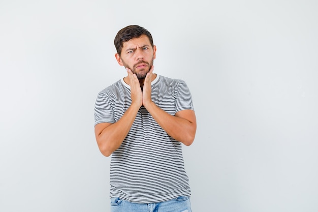 Portrait of young man touching his jaw in striped t-shirt and looking upset front view