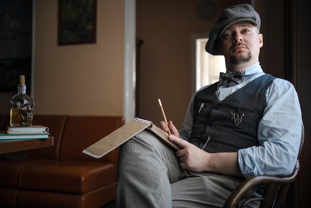 Portrait of young man in tweed vest and cap sitting with notepad in interior