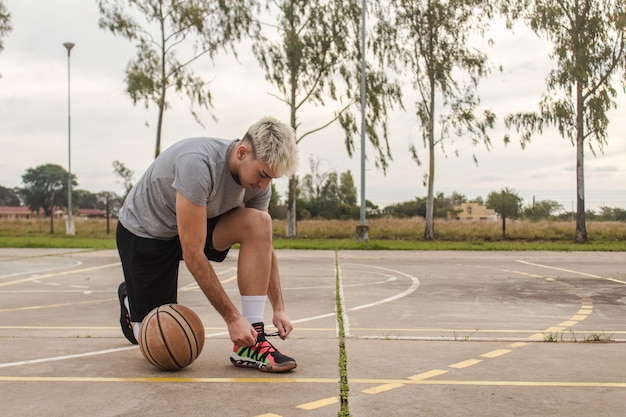 Portrait of a young man tying his shoelaces on an abandoned basketball court.