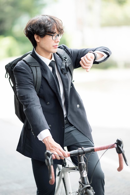 Portrait of young man wearing eyeglasses with backpack sitting on a bikecycle and look at the time on the wristwatch.