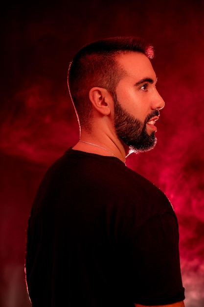 Portrait of a young man with beard on a red and black background with smoke