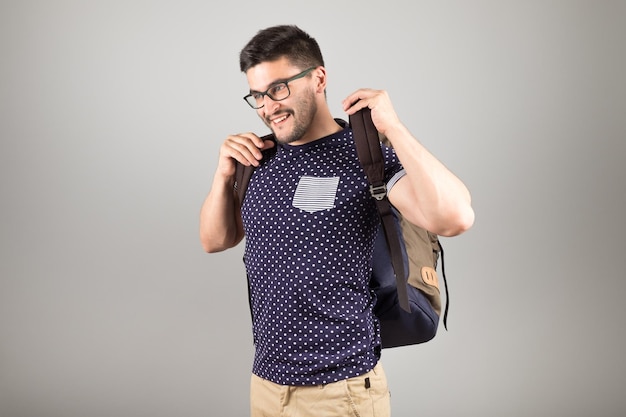 Portrait of a young man with glasses and backpack isolated on gray background