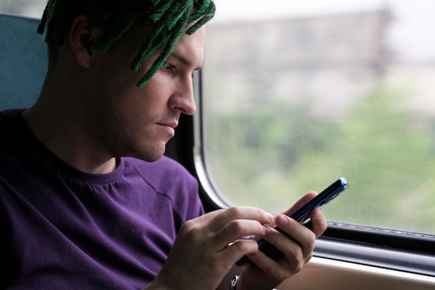 Portrait of young man with green dreadlocks browsing mobile phone riding on train Close up