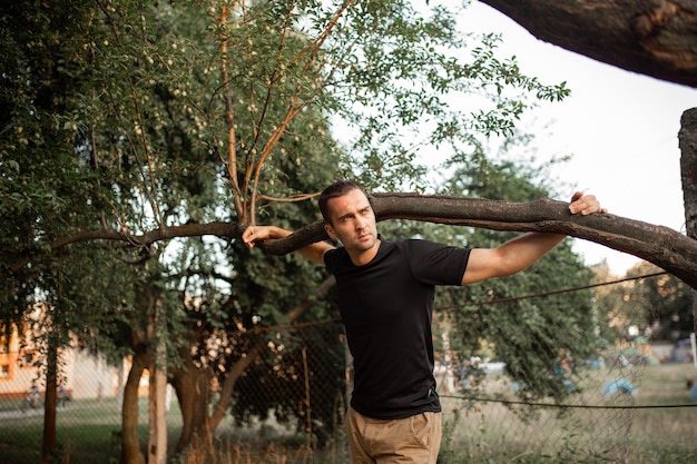 Portrait of a young man with light bristles in a black Tshirt holding a tree branch