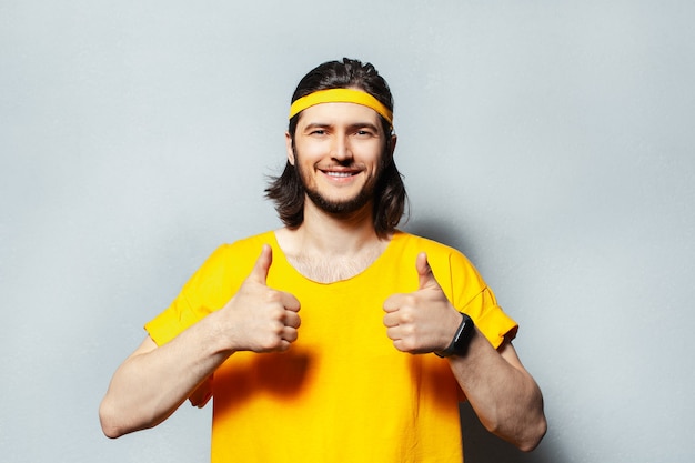 Portrait of young man in yellow shirt showing thumbs up.