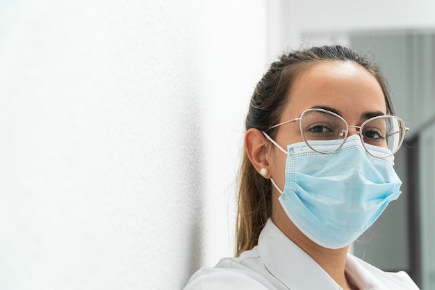 Portrait of a young masked doctor on a white surface