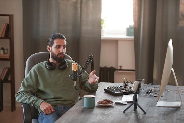 Portrait of young middle eastern influencer sitting relaxed at desk in loft room creating content fo