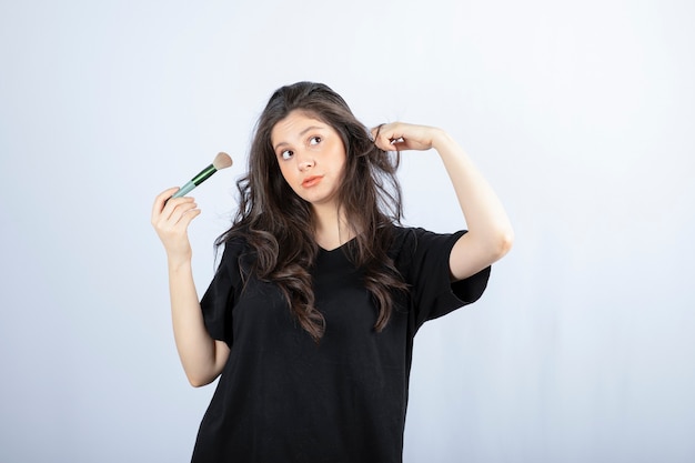 Portrait of young model with makeup with brush standing on white wall. 