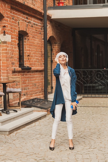 Portrait of young modern arabian woman holding mobile phone and listening the music to headphone.