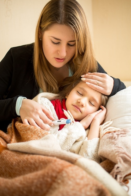 Portrait of young mother hugging sick girl in bed