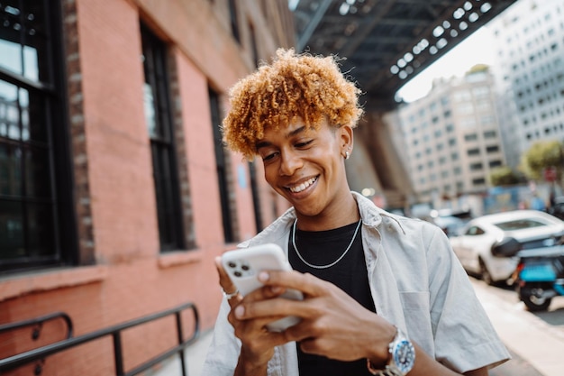 Portrait of young multiracial man smiling happy using smartphone while walking at the city curly