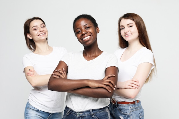 Portrait of young multiracial women standing together and smiling at camera isolated over white background