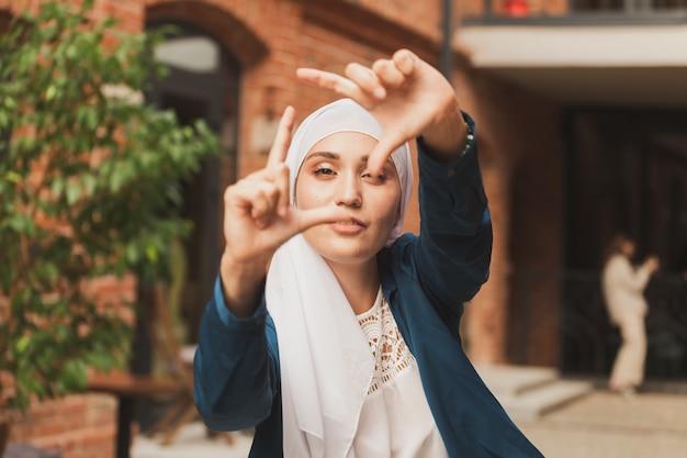 Portrait of young muslim girl making a camera frame with fingers outdoors