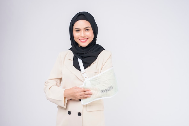 Portrait of young muslim woman with an injured arm in a sling over blue background in studio.