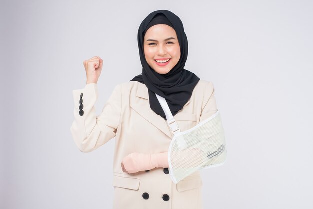 Portrait of young muslim woman with an injured arm in a sling over blue background in studio.