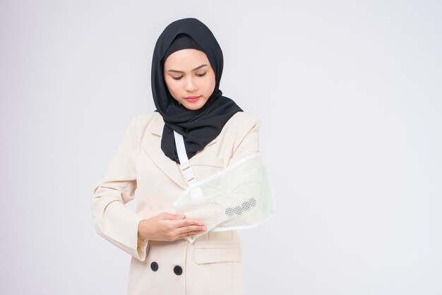 Portrait of young muslim woman with an injured arm in a sling over blue background in studio.