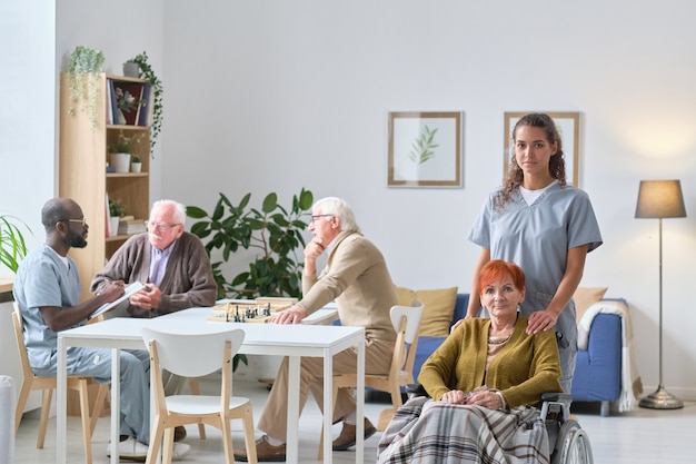 Portrait of young nurse with senior woman smiling at camera during her work in nursing home, she taking care about senior people