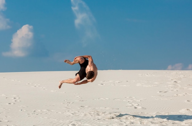 Portrait of young parkour man doing flip or somersault on the sand.