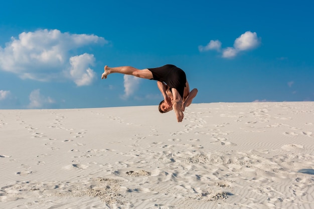 Portrait of young parkour man doing flip or somersault on the sand.