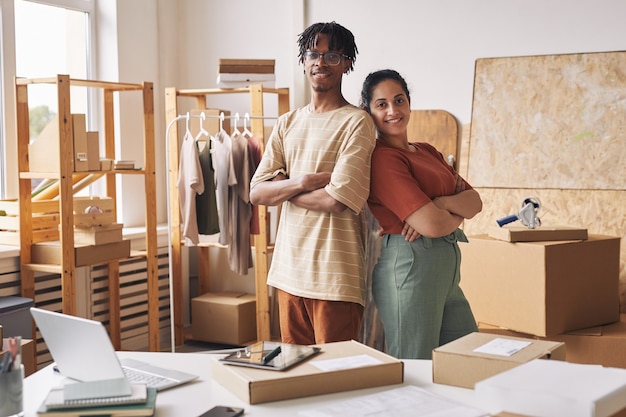 Portrait of young people standing back to back and smiling at camera while working with parcels in warehouse