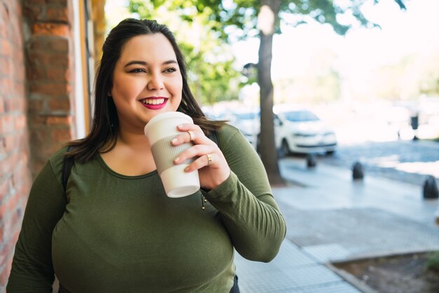 Portrait of young plus size woman holding a cup of coffee while walking outdoors