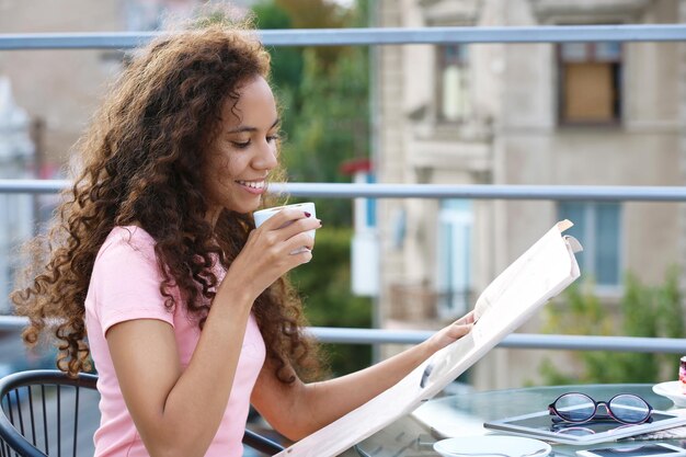 Portrait of young pretty woman reading newspaper at summer terrace in the town