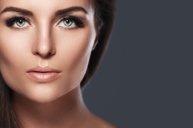 Portrait of young and pretty woman with a artificial eyelashes on dark gray background