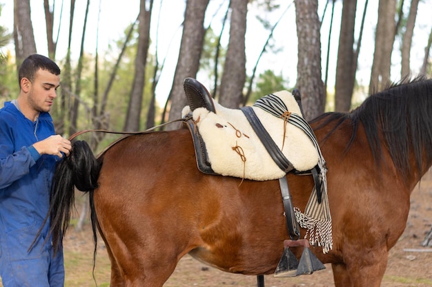 Portrait of a young rancher putting the saddle on his horse for a walk