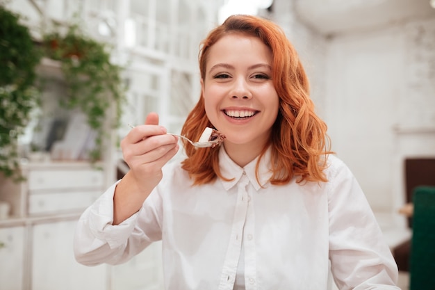 Portrait of young redhead pretty woman eating cake in cafe.