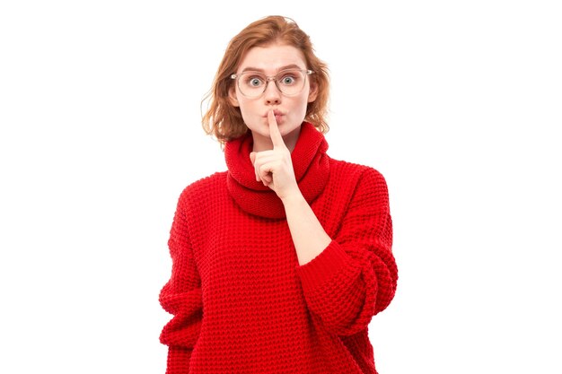 Portrait of young redhead woman covering mouth with finger isolated on white background Asks for silence keep secret shh gesture