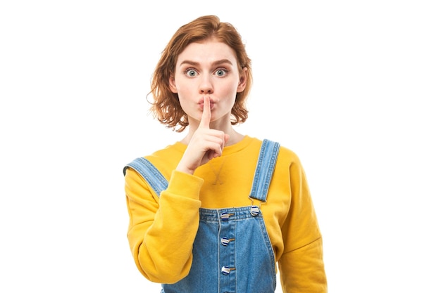 Portrait of young redhead woman covering mouth with finger isolated on white background Asks for silence keep secret shh gesture