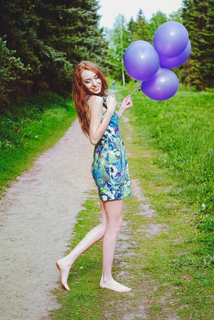 Portrait of young redhead woman in spring garden with freckles. Purple balloons. Birthday, holiday