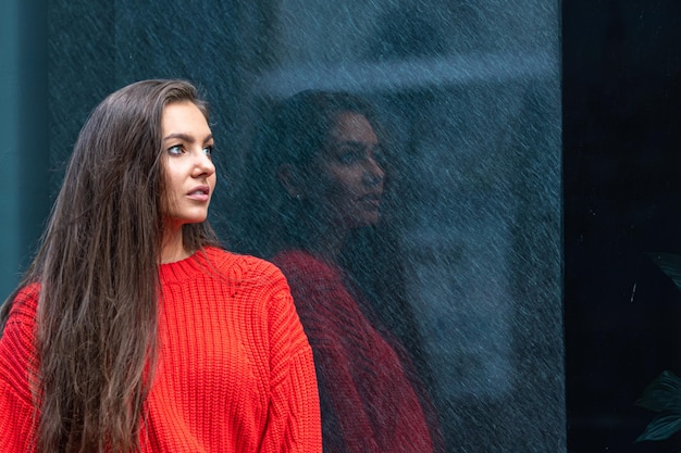 Portrait of a young sensual brunette in a red sweater by a polished dark marble wall