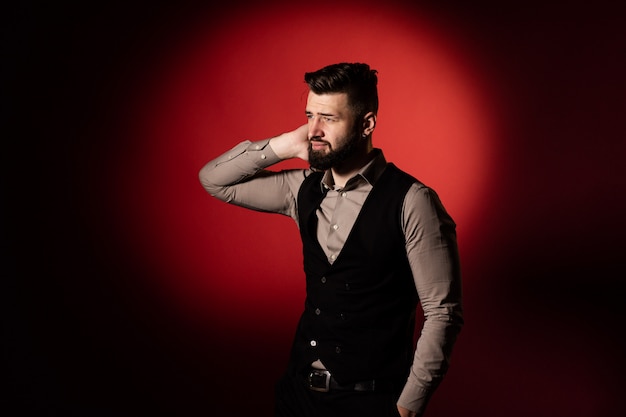 Portrait of a young serious bearded man in a black vest on red background. Space for text