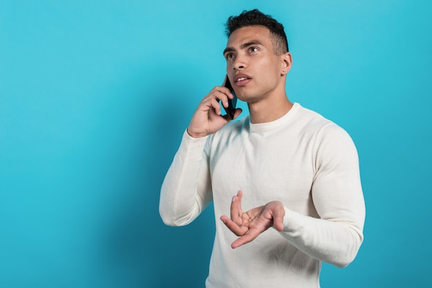 Portrait of a young serious man  in white shirt talking on smartphone and looking up 