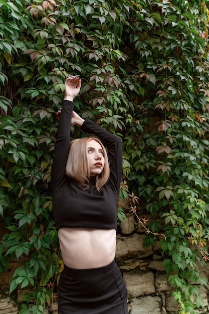 Portrait of young sexy woman in short black top on green wall with plants background Vertical frame