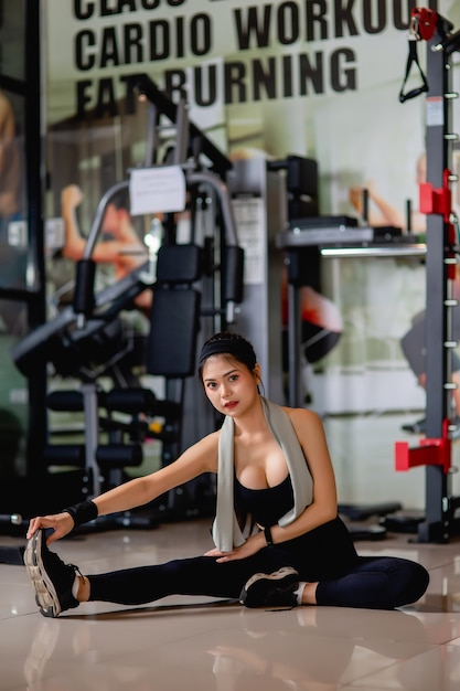 Portrait young sexy woman wearing sportswear and smartwatch sitting on floor and streching her legs muscle before workout at fitness gym, 