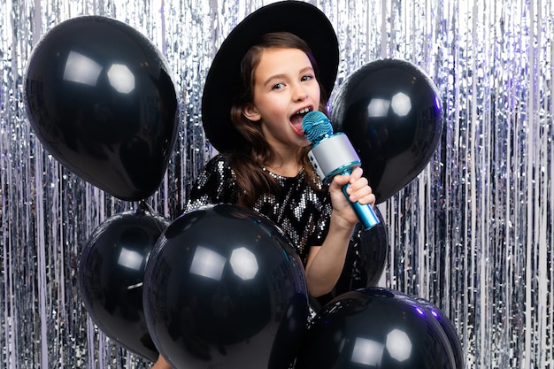 Portrait of a young singer in a black dress with a microphone in her hands on a shiny background.