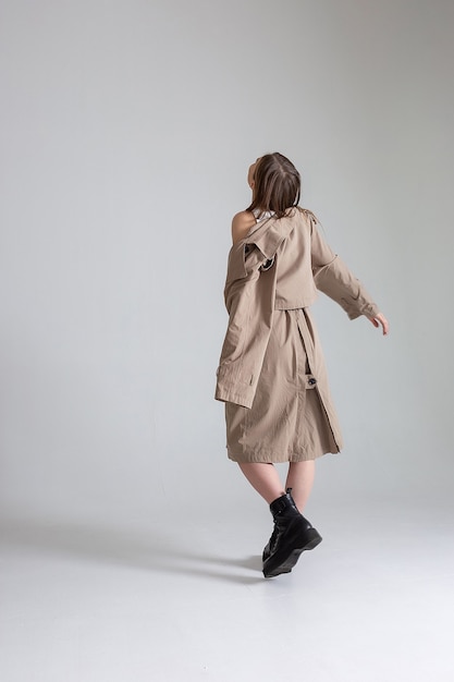 portrait of young skinny caucasian pretty girl with long hair in raincoat posing on white studio cyclorama