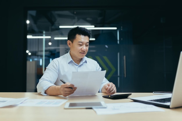 Portrait of young smiling asian male accountant banker sitting in office at desk and working on