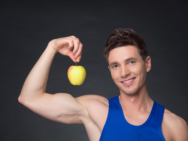 Portrait of young smiling bodybuilder holding apple in black background.