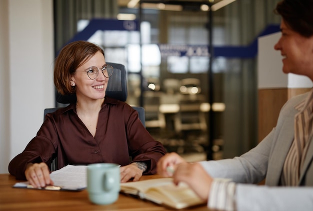 Portrait of young smiling businesswoman talking with female colleague or mentor in office copy space