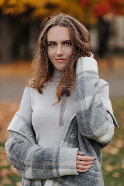 Portrait of young smiling girl in a gray dress at autumn park