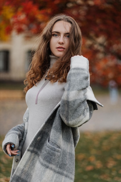 Portrait of young smiling girl in a gray dress at autumn park